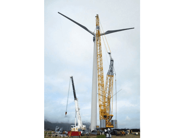 A crane is in the foreground with two wind turbines behind it.